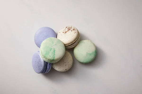 Vista superior de uma variedade de deliciosos macaroons verdes, violetas e brancos franceses no fundo cinza — Fotografia de Stock