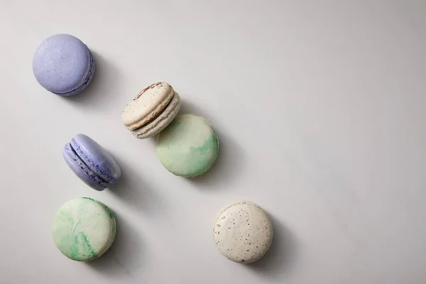 Vista superior de una variedad de deliciosos macarrones verdes, violetas y blancos franceses sobre fondo gris - foto de stock