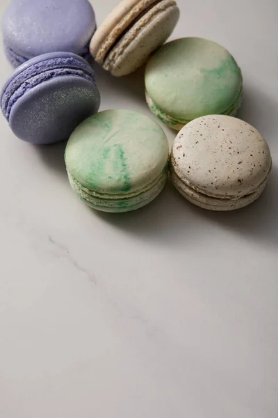 Vista de cerca de una variedad de deliciosos macarrones verdes, violetas y amarillos franceses sobre fondo gris - foto de stock