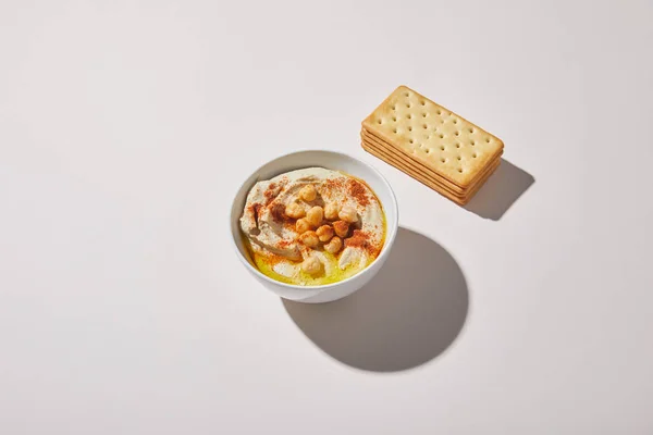 Миска з смачною гумусом біля крекерок на сірому фоні — стокове фото