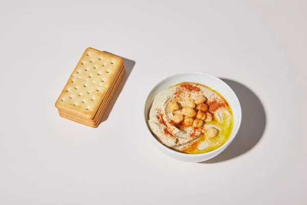 Tigela com hummus delicioso e biscoitos no fundo cinza — Fotografia de Stock