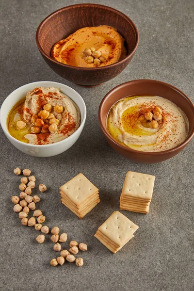 Tigelas com hummus saboroso com grão de bico e biscoitos no fundo cinza — Fotografia de Stock