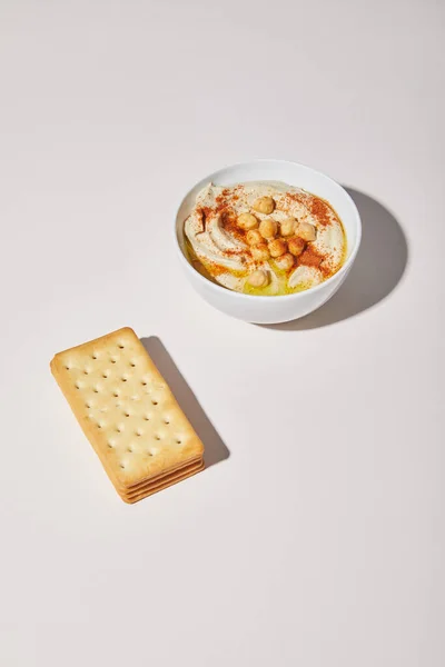 Schüssel mit leckerem Hummus und Crackern auf grauem Hintergrund — Stockfoto