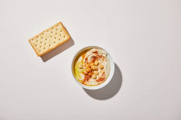 Vista superior del bowl con sabroso hummus y galletas saladas sobre fondo gris - foto de stock