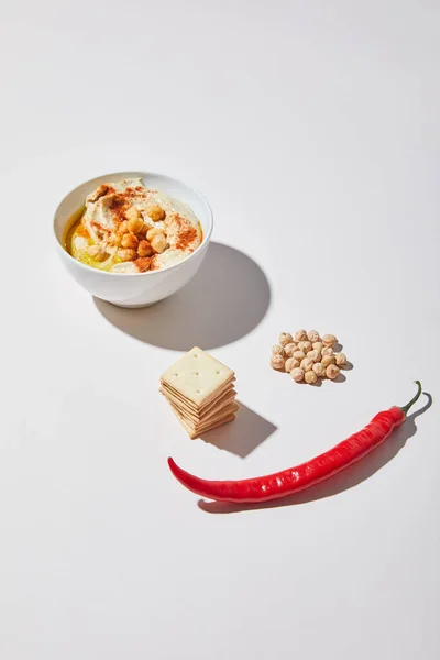 Чаша с вкусным хумусом рядом с крекерами, перец чили и горох на сером фоне — Stock Photo