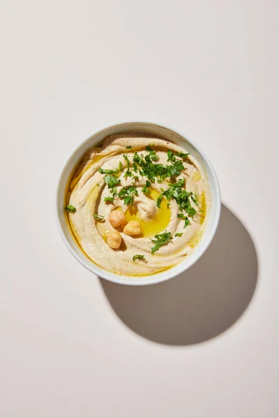 Vista superior da tigela com hummus saboroso com grão de bico e salsa sobre fundo cinza — Fotografia de Stock