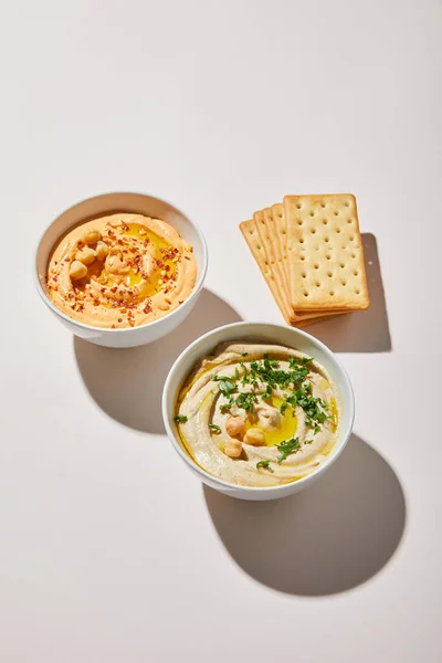 Tigelas com hummus delicioso e biscoitos no fundo cinza — Fotografia de Stock