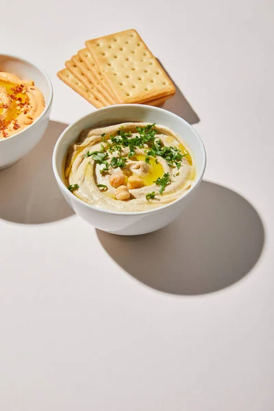 Bowls with tasty hummus and crackers on grey background — Stock Photo