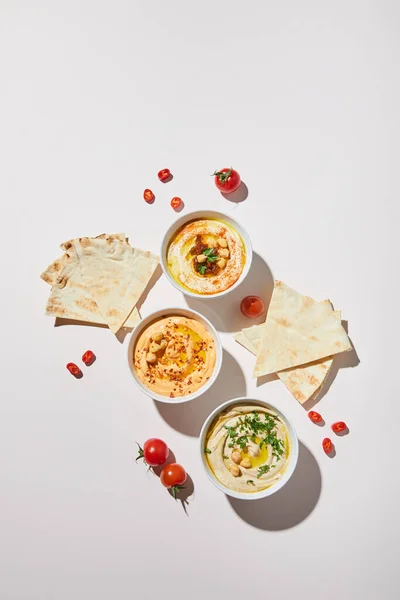 Draufsicht auf Schalen mit köstlichem Hummus, reifem Gemüse und Fladenbrot auf grauem Hintergrund — Stockfoto