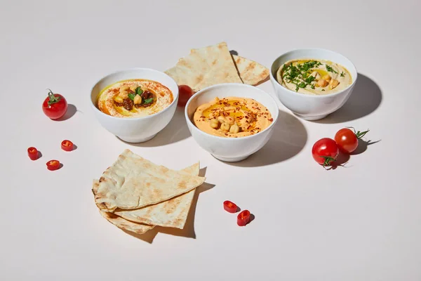 Bowls with hummus, ripe vegetables and pita bread on grey background — Stock Photo