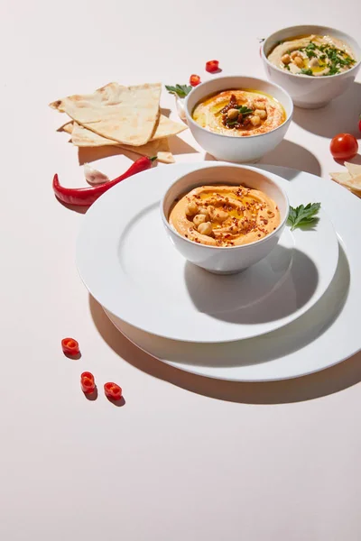 Selective focus of plates and bowls with hummus, vegetables and pita bread on grey — Stock Photo