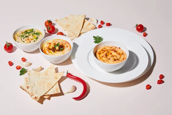 Plates and bowls with hummus, fresh vegetables and pita bread on grey — Stock Photo