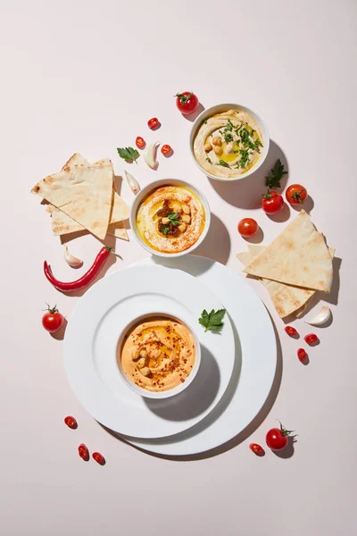 Draufsicht auf Teller und Schalen mit Humus, frischem Gemüse und Fladenbrot auf grauem Hintergrund — Stockfoto