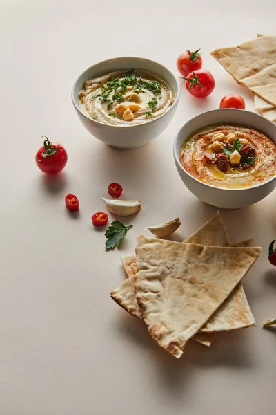 Bowls with hummus, fresh vegetables and pita bread on grey — Stock Photo