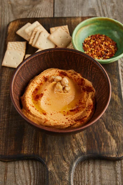 Concentration sélective de craquelins, bols avec paprika et houmous sur planche à découper sur fond en bois — Photo de stock