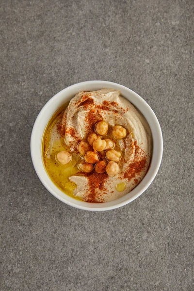Vista superior da tigela com delicioso hummus com grão de bico e azeite sobre fundo cinza — Fotografia de Stock