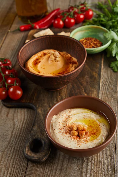 Selective focus of bowls with paprika and hummus, vegetables and parsley on wooden background — Stock Photo