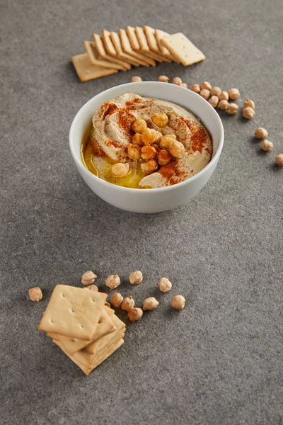 Hummus delicioso em tigela com grão de bico e biscoitos no fundo cinza — Fotografia de Stock
