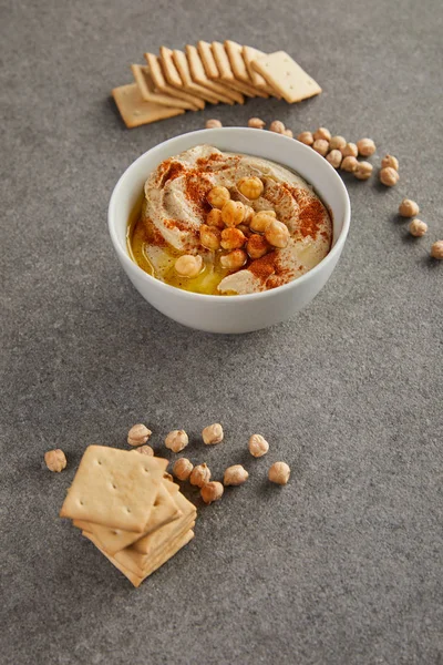 Délicieux houmous dans un bol avec pois chiches et craquelins sur fond gris — Photo de stock