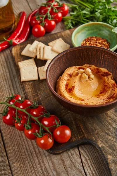 Selective focus of bowls with hummus and spices, ripe vegetables and crackers on wooden background — Stock Photo
