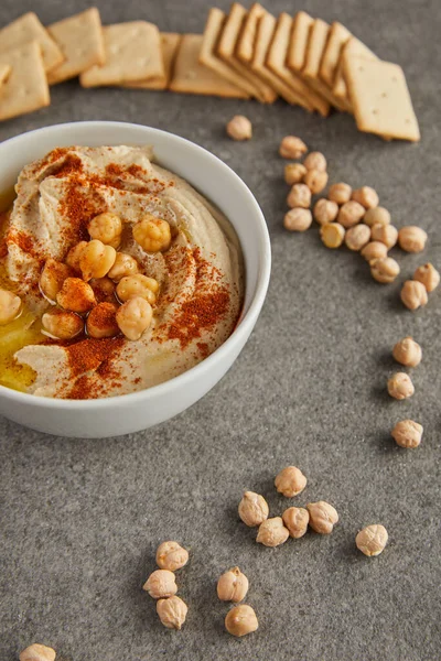 Selektiver Fokus der Schale mit leckerem Humus, Kichererbsen und Crackern auf grauem Hintergrund — Stockfoto