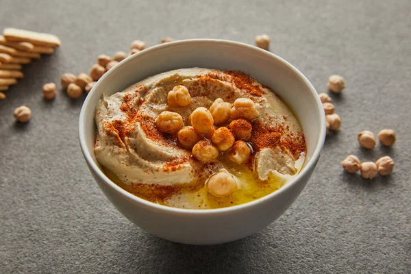 Vista de perto da tigela com hummus saboroso, grão de bico e biscoitos no cinza — Fotografia de Stock