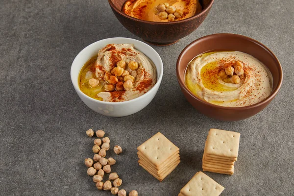 Bowls with delicious hummus with chickpea and crackers on grey background — Stock Photo
