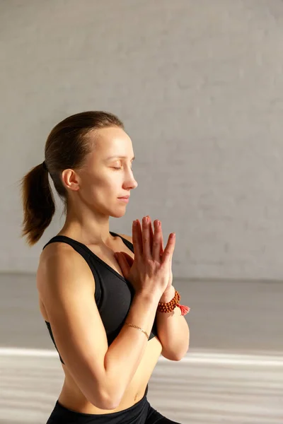 Femme attrayante avec les yeux fermés et les mains priantes dans le studio de yoga — Photo de stock