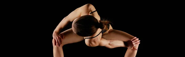 Tiro panorâmico de menina fazendo girado ângulo lateral limitado exercício isolado em preto — Fotografia de Stock