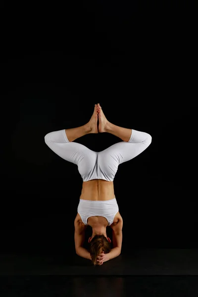 Back view of girl in white sportswear doing baddha konasana in handstand isolated on black — Stock Photo