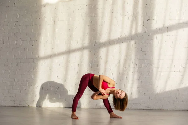 Mulher esportiva com descalço fazendo exercício de ioga perto da parede de tijolo — Fotografia de Stock