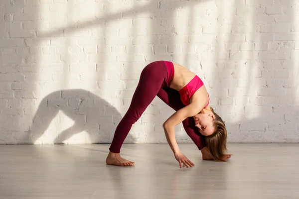 Chica deportiva con descalzo haciendo ejercicio de yoga cerca de la pared de ladrillo - foto de stock