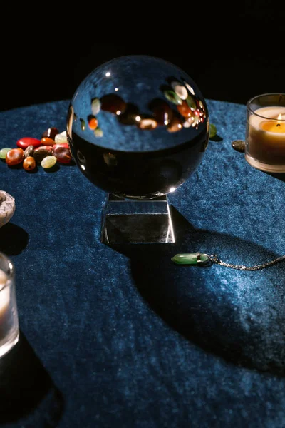 Crystal ball, candles and fortune telling stones on dark blue velour cloth isolated on black — Stock Photo