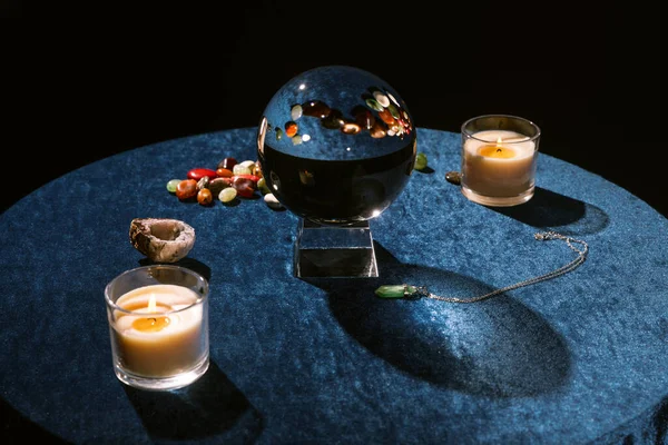 Crystal ball near candles and fortune telling stones on dark blue velour cloth isolated on black — Stock Photo