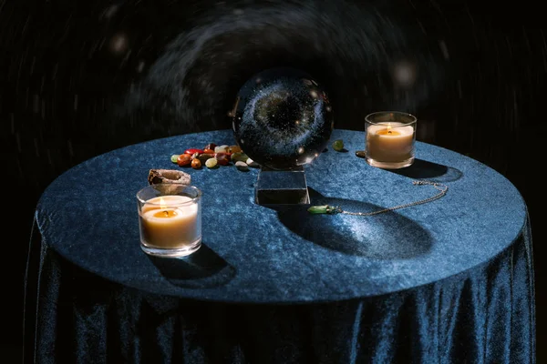 Boule de cristal près des bougies et de la fortune racontant des pierres sur tissu velours bleu foncé sur noir — Photo de stock