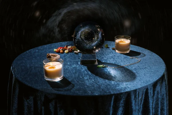 Bola de cristal perto de velas e fortuna dizendo pedras em pano de veludo azul escuro em preto — Fotografia de Stock
