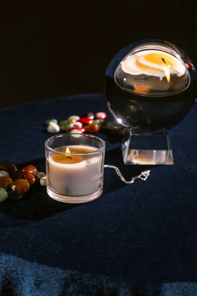 Selective focus of crystal ball, candle, fortune telling stones on dark blue velour fabric isolated on black — Stock Photo