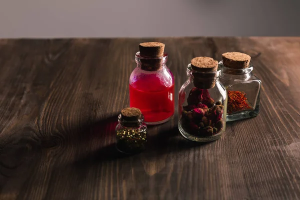 Jars with pink buds, dried herbs and magic tincture on wooden and grey background — Stock Photo