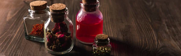 Jars with pink buds, dried herbs and magic tincture on wooden background, panoramic shot — Stock Photo