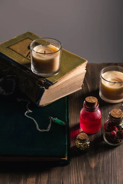 Jars with herbs and tincture near books and candles on wooden and grey background — Stock Photo