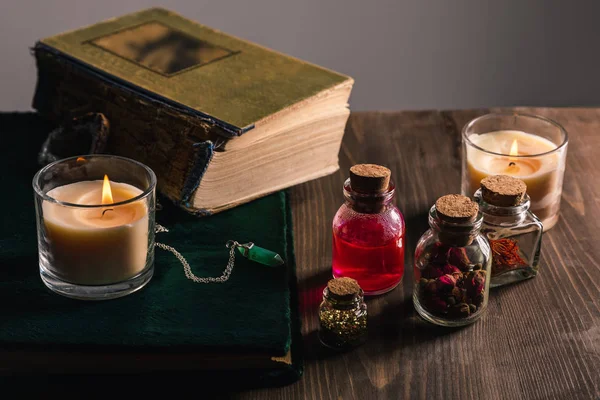 Frascos con hierbas y tintura, libros, velas sobre fondo de madera y gris - foto de stock