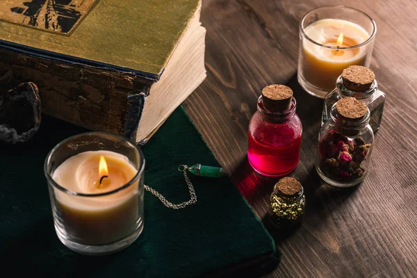 Frascos com ervas mágicas e tintura, livros e velas sobre fundo de madeira — Fotografia de Stock