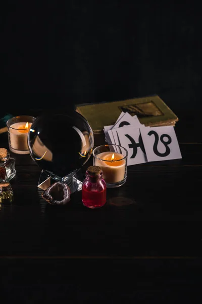 Crystal ball with mystical and occult objects on wooden and black background — Stock Photo