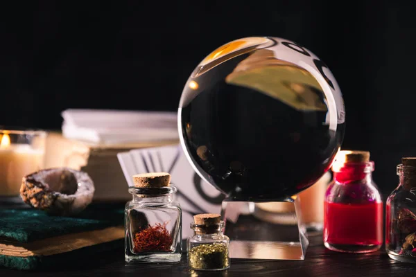 Selective focus of crystal ball with jars of dried herbs and tincture isolated on black — Stock Photo
