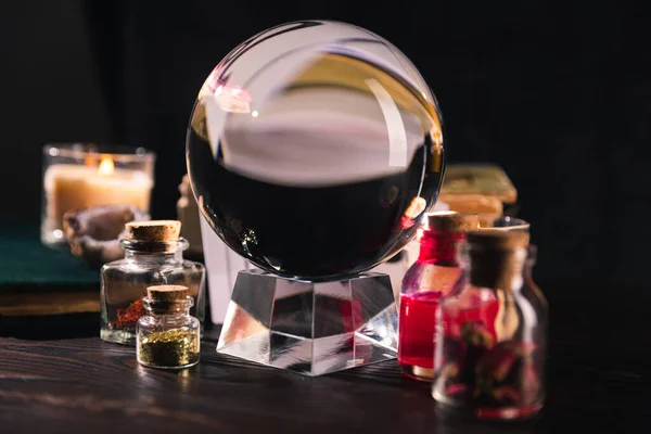 Selective focus of crystal ball with jars of dried herbs and tincture on black background — Stock Photo