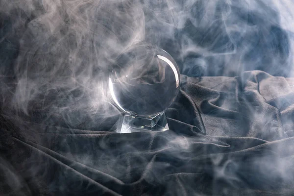 Bola de cristal sobre têxteis com fumaça em torno de fundo escuro — Fotografia de Stock