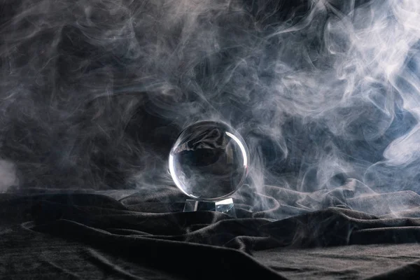 Crystal ball on black textile with smoke on dark background — Stock Photo