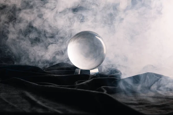 Bola de cristal sobre tecido com fumaça no fundo escuro — Fotografia de Stock