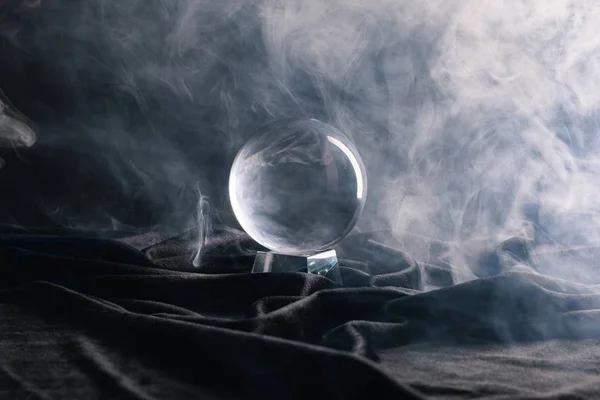 Crystal ball on black textile with smoke on dark — Stock Photo