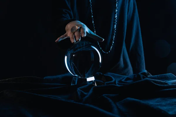 Cropped view of female hand touching crystal ball on black background — Stock Photo